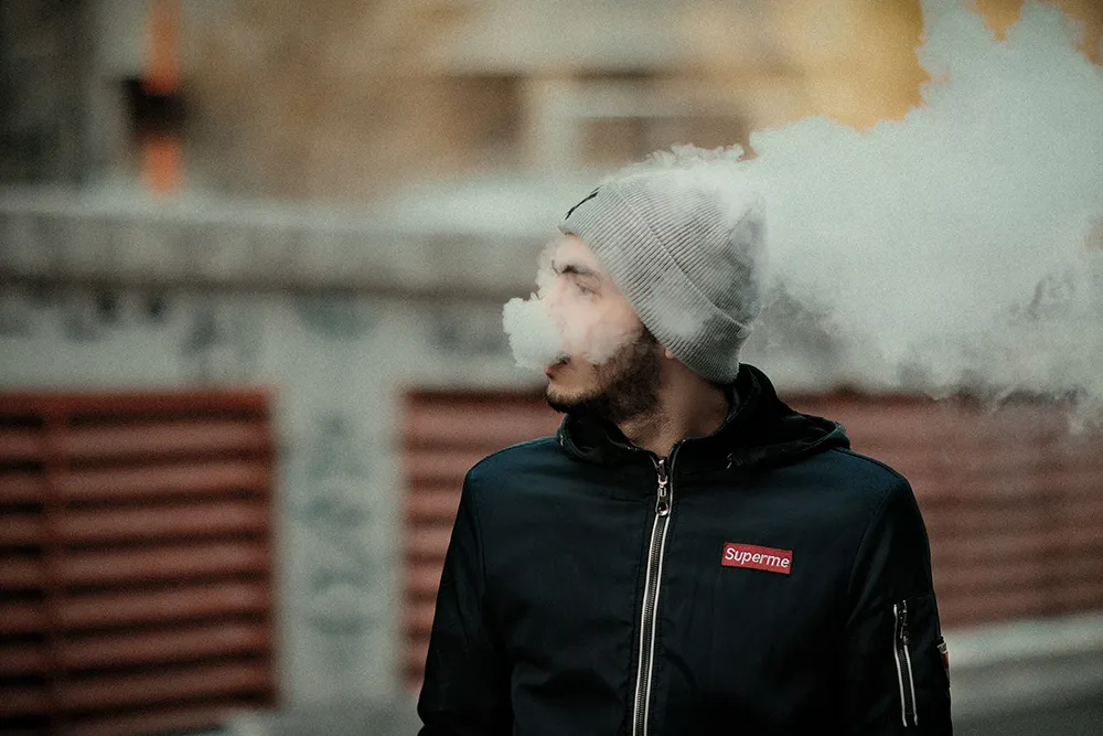 戴灰色毛帽的男子在戶外吐出電子煙蒸氣